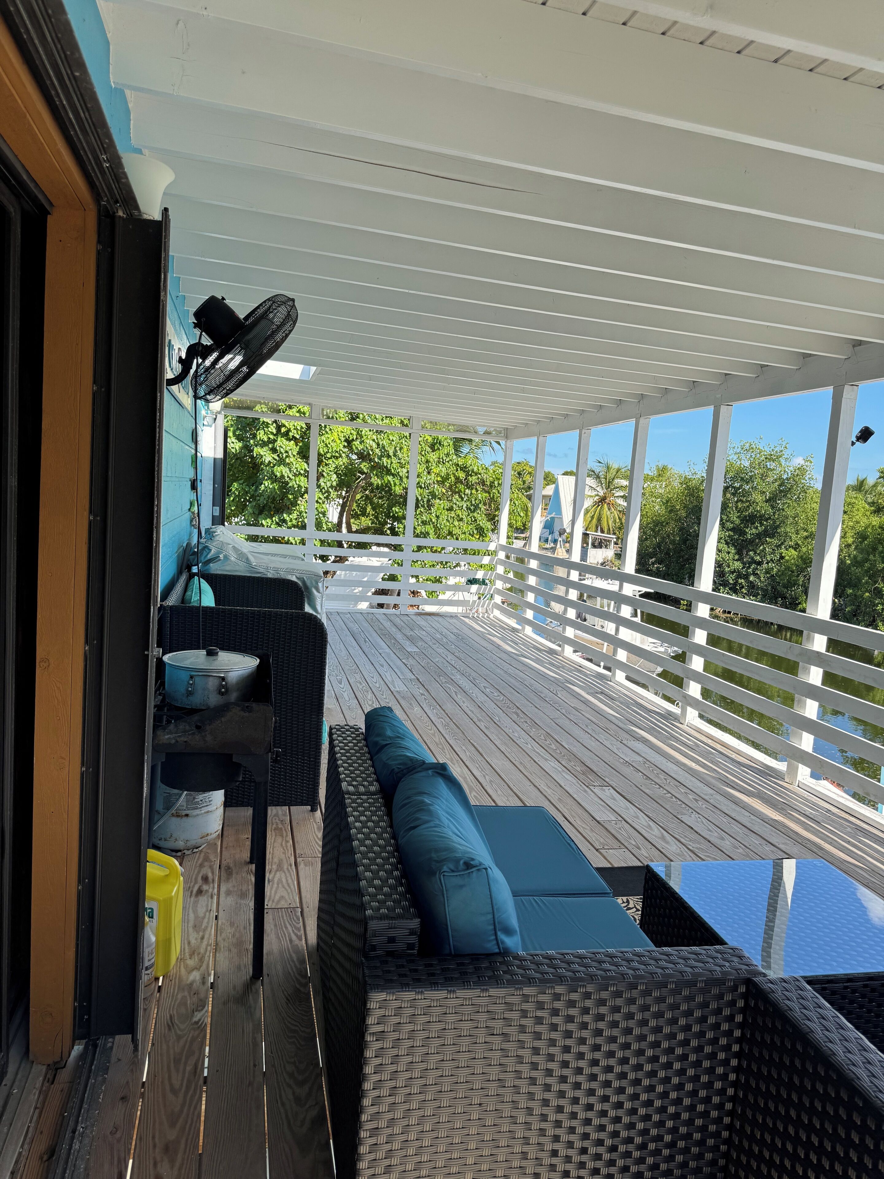 Eine überdachte Terrasse im Freien mit Korbmöbeln, einem Ventilator und Blick auf die umliegende Grünfläche.
