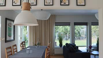Uma sala de jantar com mesa posta para quatro pessoas, um sofá e uma janela grande com vista para o verde.