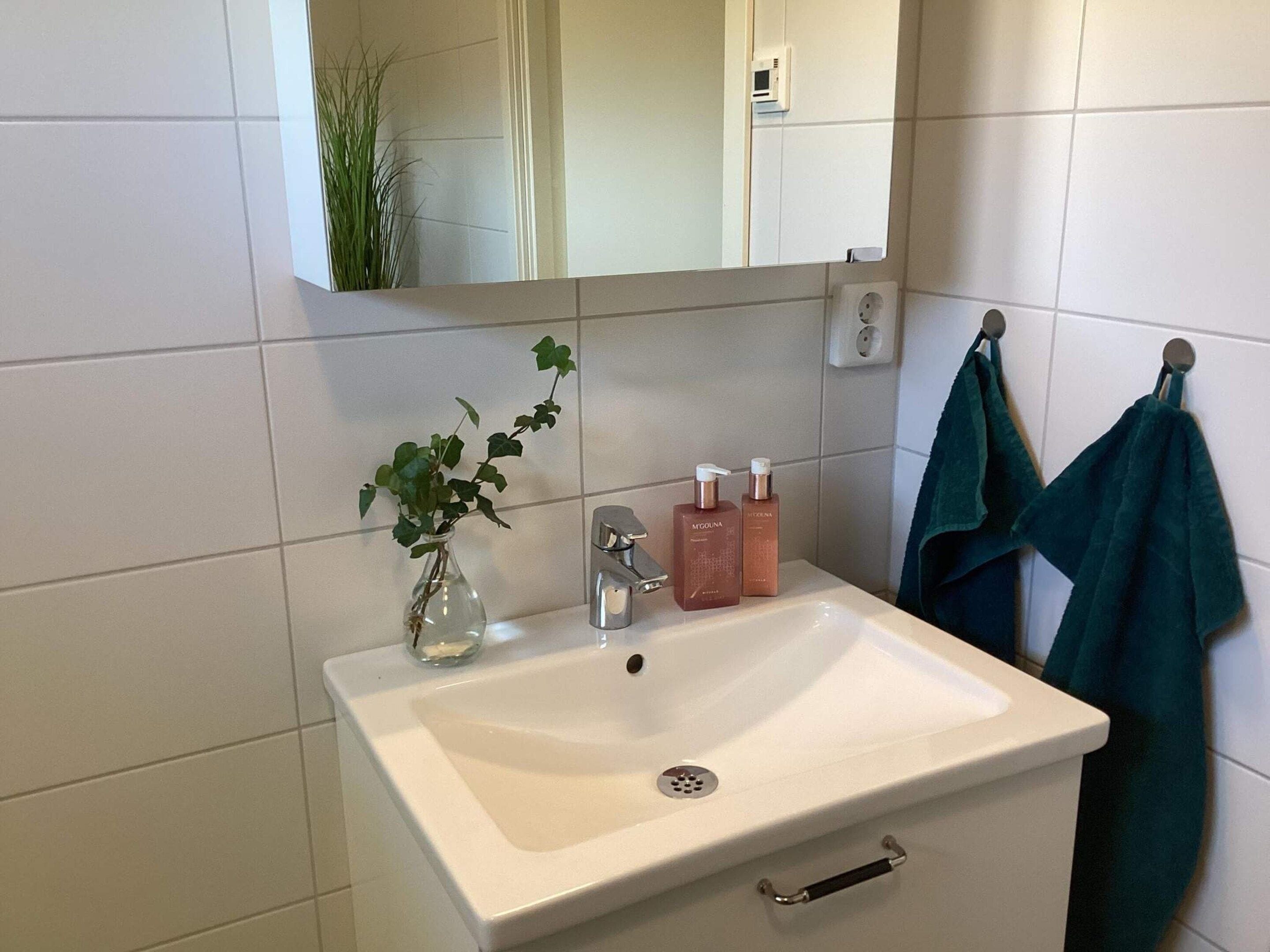 A bathroom with a white sink, a mirror, a green towel, and a potted plant.