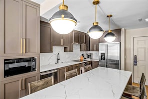 A modern kitchen with dark brown cabinets, stainless steel appliances, and a marble island. - Ski-In / Ski-Out Designer Westgate Condo | Soaking Tub | Fireplace | Patio | Spa (Park City)