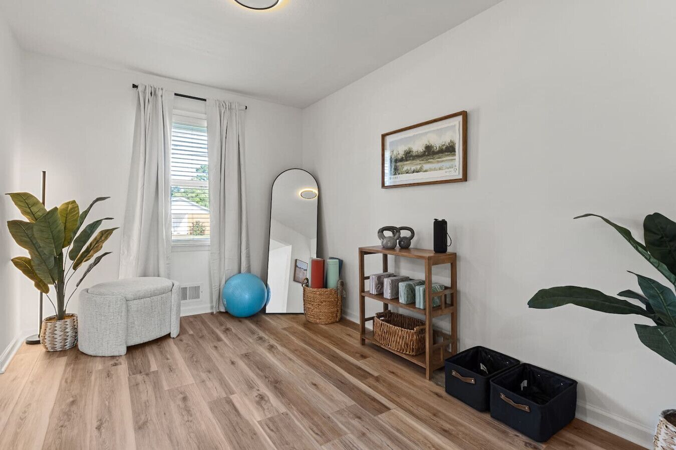 Una habitación con suelo de madera, un espejo grande, una estantería con equipo de ejercicio y un cuadro enmarcado en la pared.