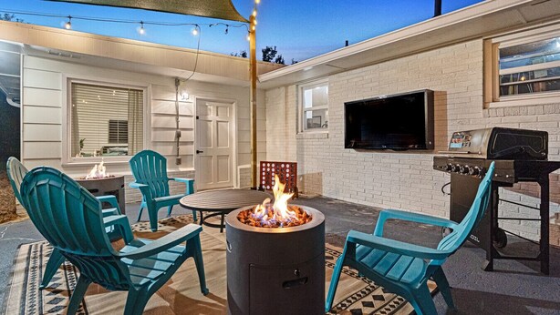 Een terras buiten met een vuurkorf, zitplaatsen buiten, een barbecue en een televisie aan de muur.