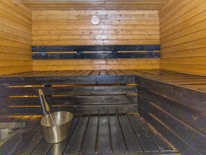 A sauna with wooden walls, a bench, and a metal bucket.
