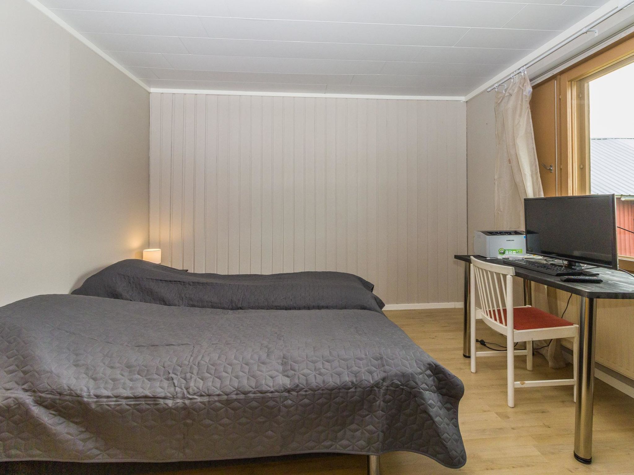 Una habitación pequeña y ordenada con una cama, un escritorio con una computadora y una silla.