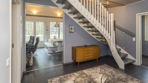 Een modern interieur met een trap naar een tweede verdieping, een houten kast en een eethoek met uitzicht op het buitenlandschap.