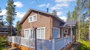 Een houten huis met twee verdiepingen, voorzien van een witte veranda en terras, omgeven door bomen.