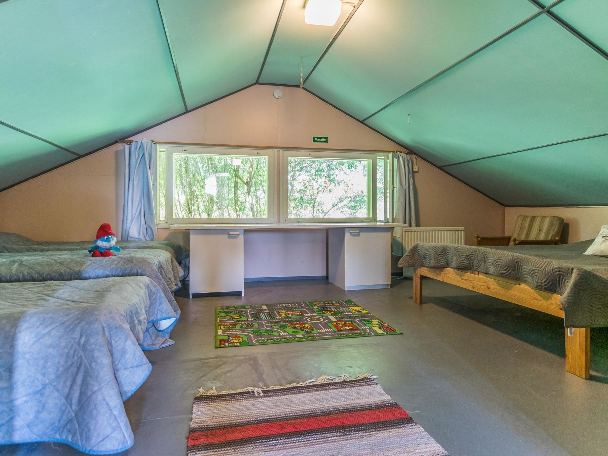 Une chambre mansardée chaleureuse, dotée de deux lits, d’un bureau et d’une fenêtre donnant sur un paysage verdoyant.