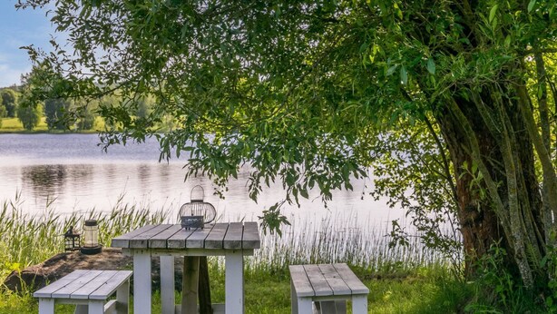 Une table de pique-nique en bois, avec deux bancs et une lanterne, installée sur l’herbe, près d’un lac.