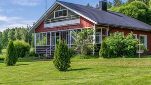 Une maison rouge avec une grande véranda, entourée de pelouse verdoyante et d’arbres.