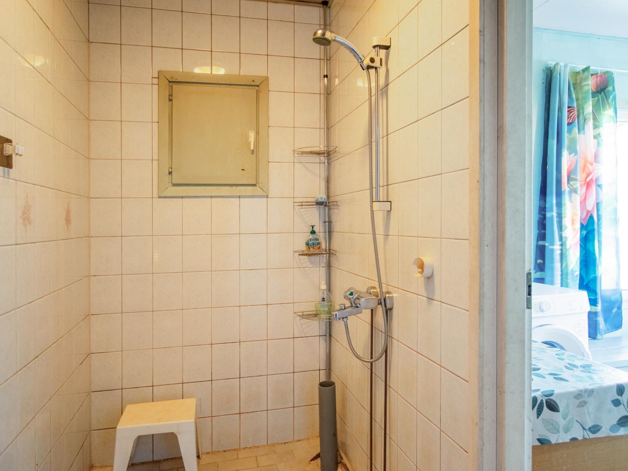 Un baño pequeño con azulejos, una ducha, un taburete pequeño y un espejo.