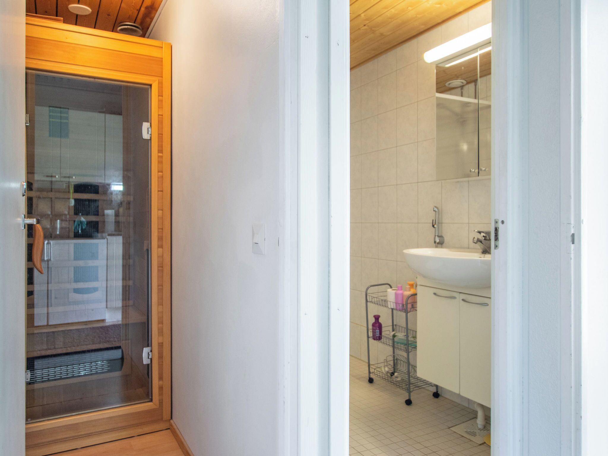 A modern bathroom with a glass shower enclosure, a white sink, and a metal cart with toiletries.