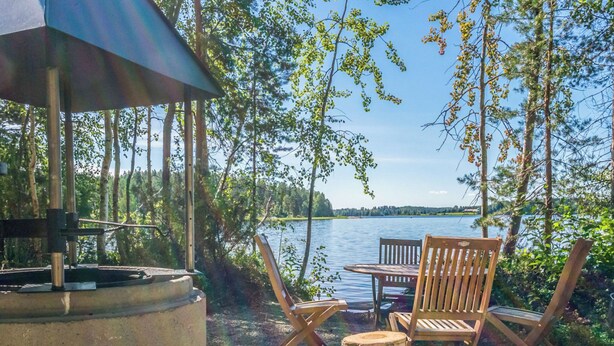 Ein Sitzbereich im Freien am Seeufer mit Grill, Holzstühlen und einem Tisch.
