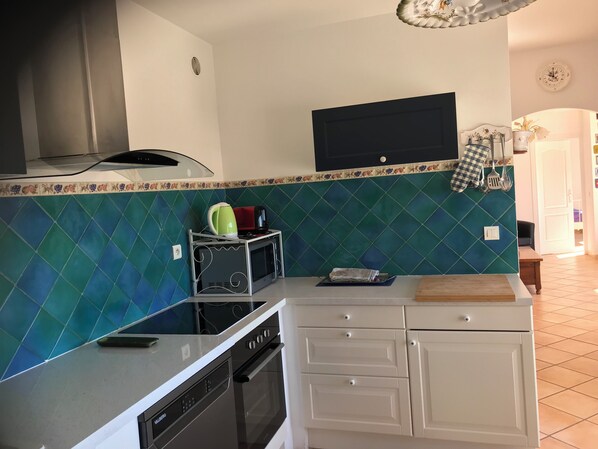 Une cuisine moderne équipée d’un four à micro-ondes, d’une cuisinière et d’un four. Un téléviseur est fixé au-dessus du comptoir, et un revêtement mural décoratif agrémente l’espace.