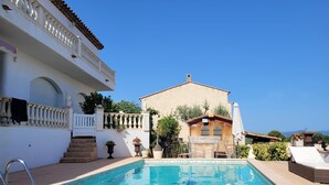 A swimming pool with a white building in the background, a wooden deck, and a clear blue sky.