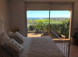 Une chambre à coucher avec un lit, des coussins à motifs, une vue sur un vignoble et un balcon doté d’une balustrade.