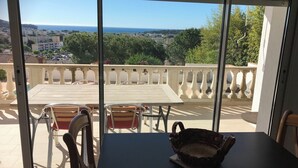 A balcony with a table and chairs, overlooking a residential area and the sea.