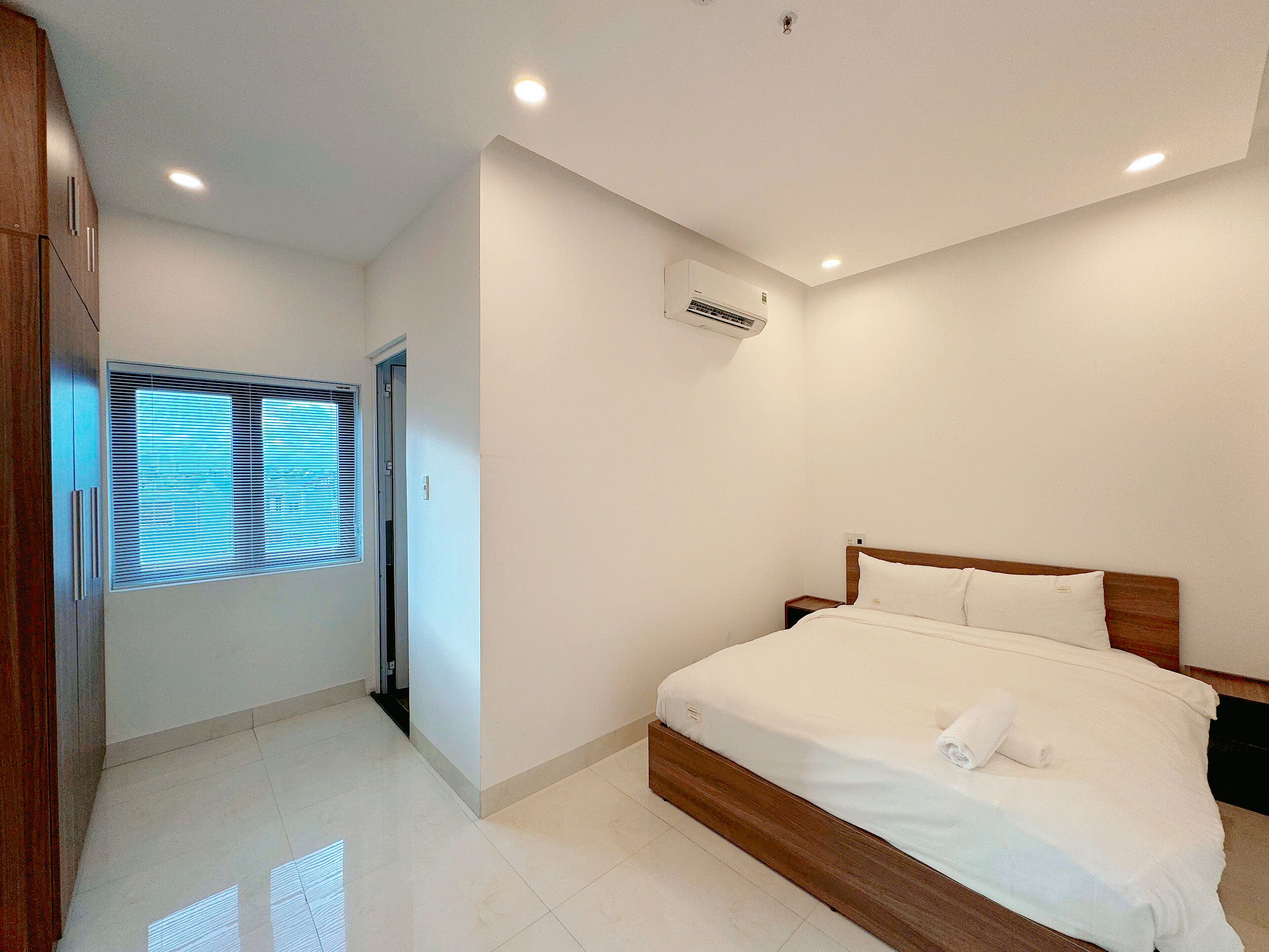 Un dormitorio con cama de madera, ropa de cama blanca y ventana con persianas.