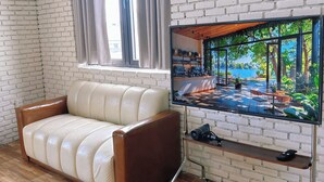 A living room with a leather sofa, a flat-screen TV mounted on a brick wall, and a window with curtains. - Ania Beachside Hotel Da Nang (Da Nang)
