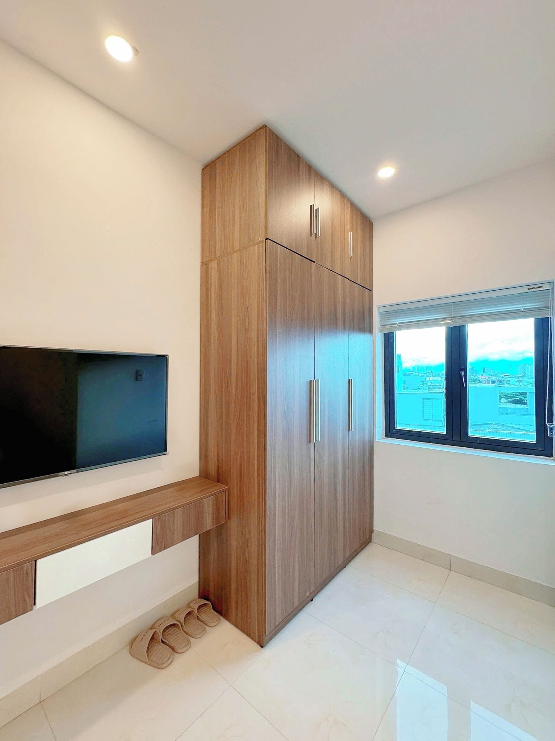 A modern room with a built-in TV, wooden wardrobe, and a window with a city view.
