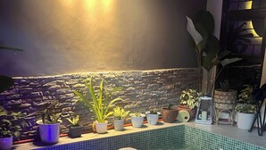 Ein Pool mit Wasserspiel, umgeben von Kübelpflanzen und einer Steinmauer.