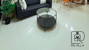Ein modernes Wohnzimmer mit einer Couch, einem Glastisch, einem Essbereich mit Stühlen, einem Ventilator und einer Treppe im Hintergrund.