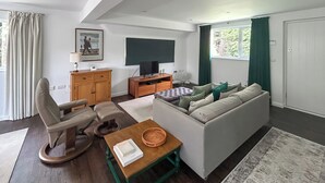 A modern living room with a sofa, a chair, a wooden cabinet, a television, and a window with curtains. - 1 bedroom accommodation in Horsham, near Brighton (Horsham, near Brighton)