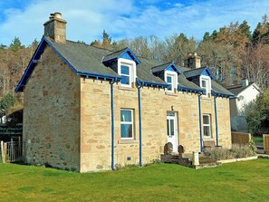 A stone house with a gabled roof, multiple windows, and a chimney.