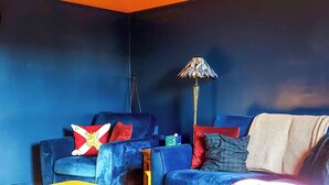 Une pièce avec deux canapés bleus, un pouf jaune et une lampe.