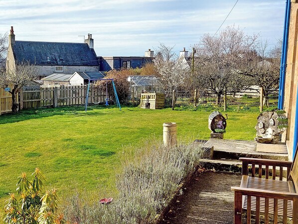 A residential garden with a lawn, a swing set, a wooden fence, and a greenhouse.