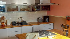 Une cuisine avec des meubles blancs, un plan de travail en bois, une cuisinière à gaz, une machine à café et un évier.