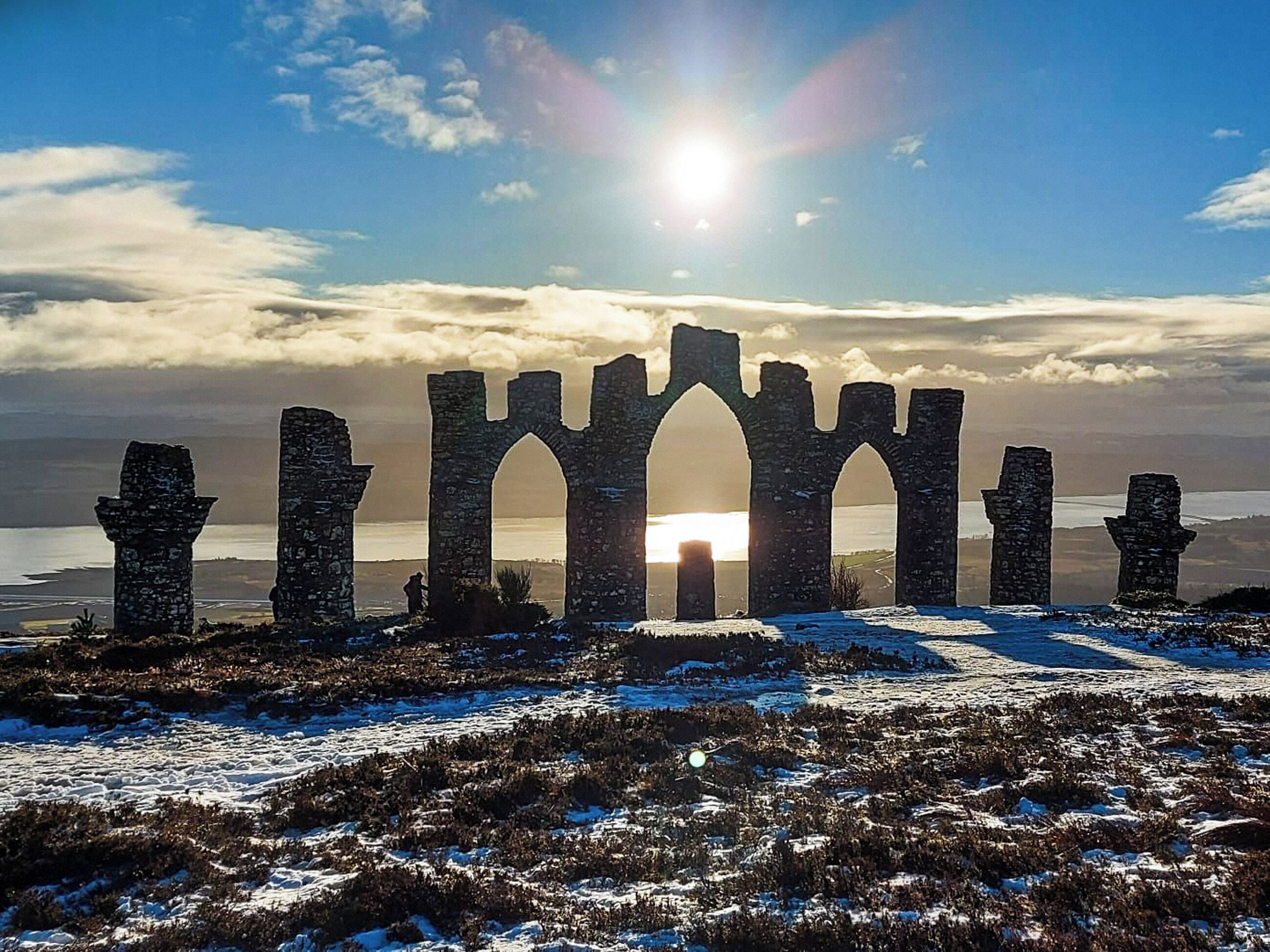 Una estructura de piedra histórica con arcos y columnas, frente a un cielo despejado y una masa de agua.