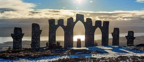 Una estructura de piedra histórica con arcos y columnas, frente a un cielo despejado y una masa de agua.