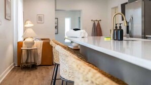A modern kitchen with a white countertop, stainless steel appliances, and a bar stool.