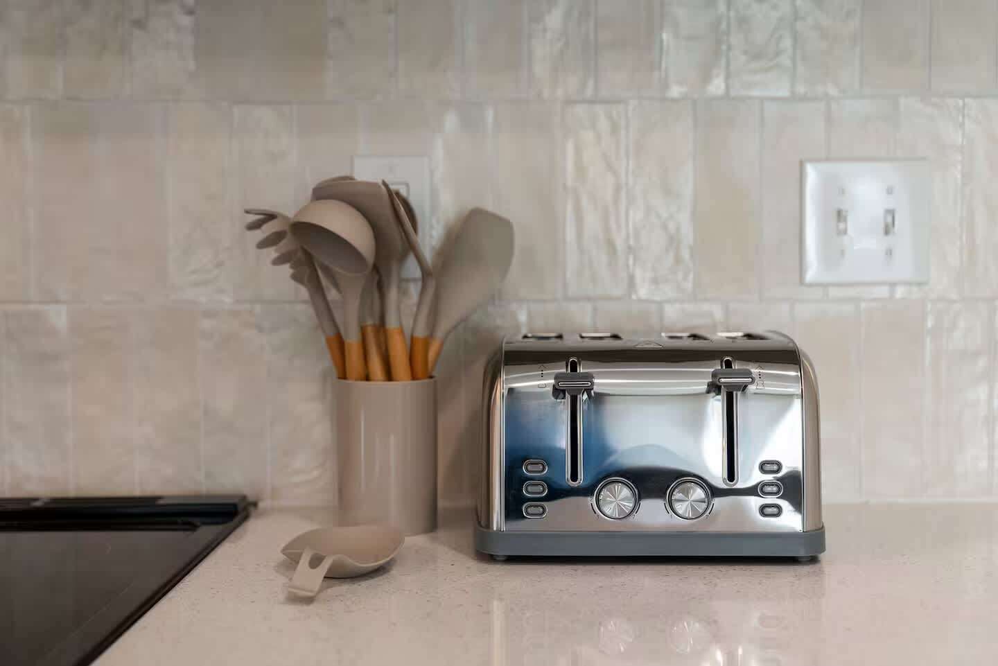 A kitchen with a toaster, a white mug with utensils, and a white countertop.