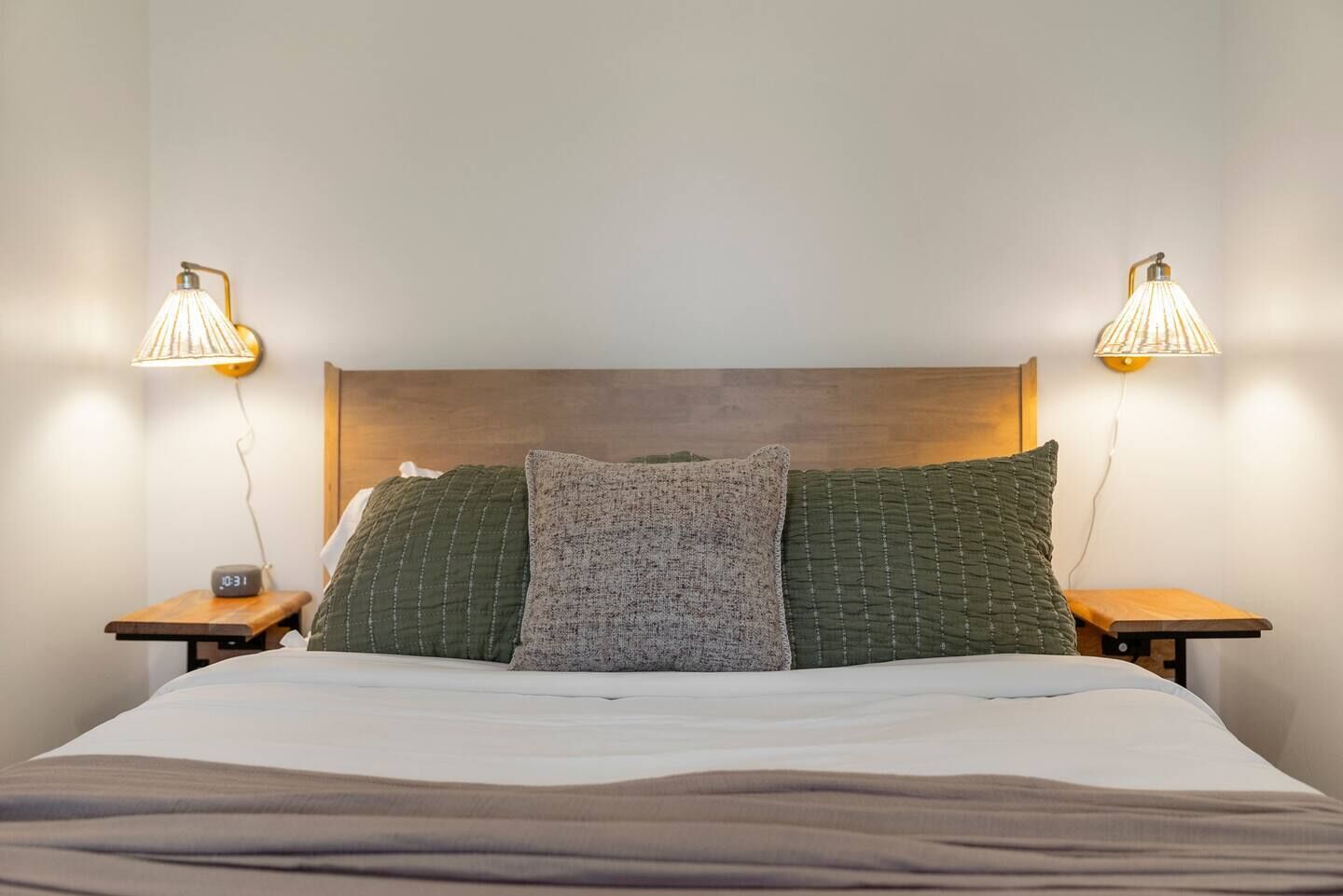 A neatly made bed with a wooden headboard, two bedside tables with lamps, and a digital clock.
