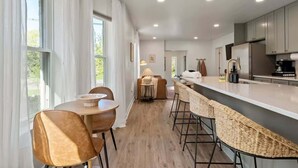 A modern kitchen with a bar area, wooden flooring, and large windows.