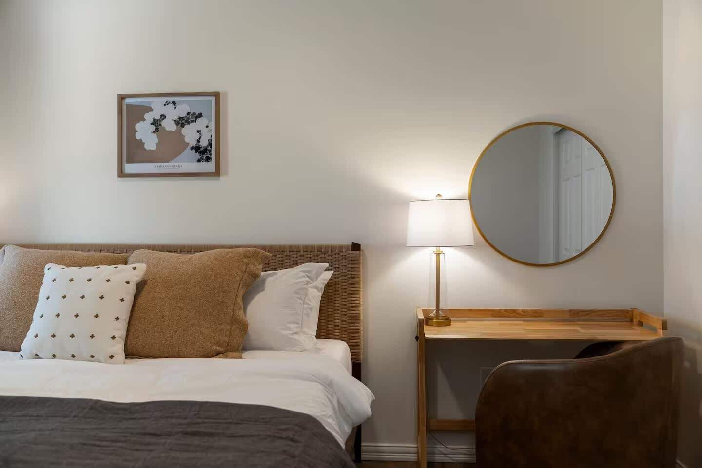 Habitació d'hotel ordenada amb llit, una taula de nit amb làmpada, una cadira i un mirall rodó penjat a la paret.