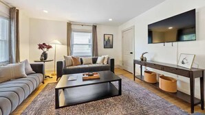 A modern living room with a sofa, coffee table, and a TV mounted on the wall. - Close to OSU Rooftop Patio  Grill & Outdoor TV (Columbus)