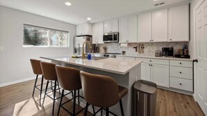 Una cocina moderna con gabinetes blancos, electrodomésticos de acero inoxidable y una isla central con taburetes de bar.