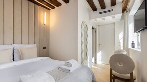 Une chambre d’hôtel moderne, dotée d’un grand lit, d’une chaise, d’un miroir et d’un téléviseur fixé au mur.