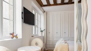 Une pièce avec un plafond en bois, un lit recouvert d’une couette blanche, une table ronde avec des chaises et un grand miroir au mur.