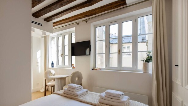 Une chambre à coucher comprenant un lit, un bureau, une chaise, un téléviseur et de grandes fenêtres.