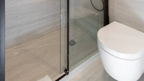Une salle de bain moderne avec une douche  à parois de verre, des toilettes blanches et un panneau de commande fixé au mur.