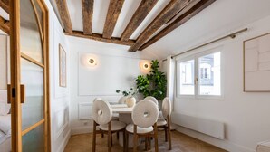 Ein Essbereich mit Holzboden, weißen Wänden und einem Fischgrätparkett. Es steht ein Tisch mit vier Stühlen und einem Blumentopf darauf.