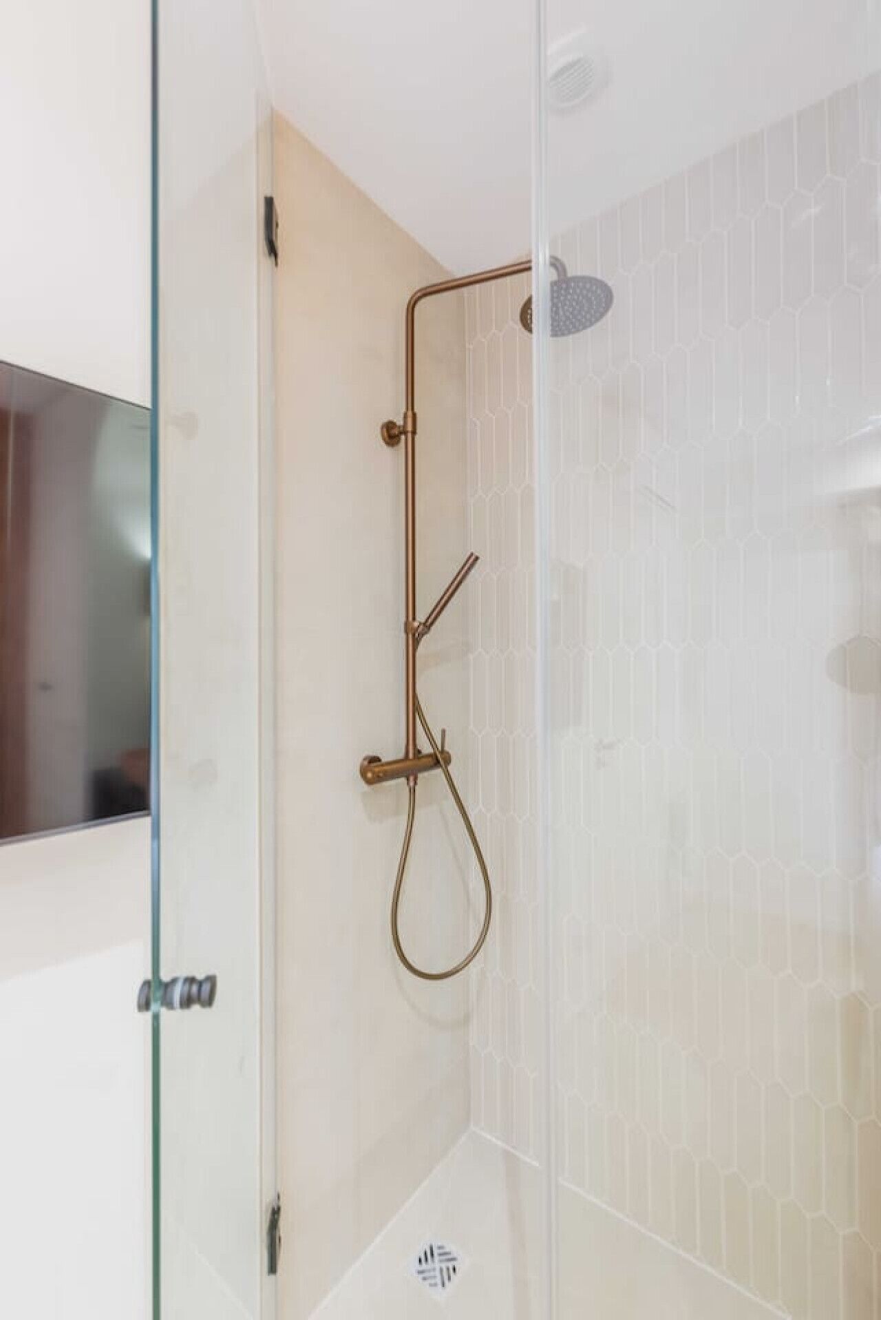 A modern shower with a glass door, a handheld showerhead, and a wall-mounted control.
