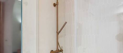 A modern shower with a glass door, a handheld showerhead, and a wall-mounted control.