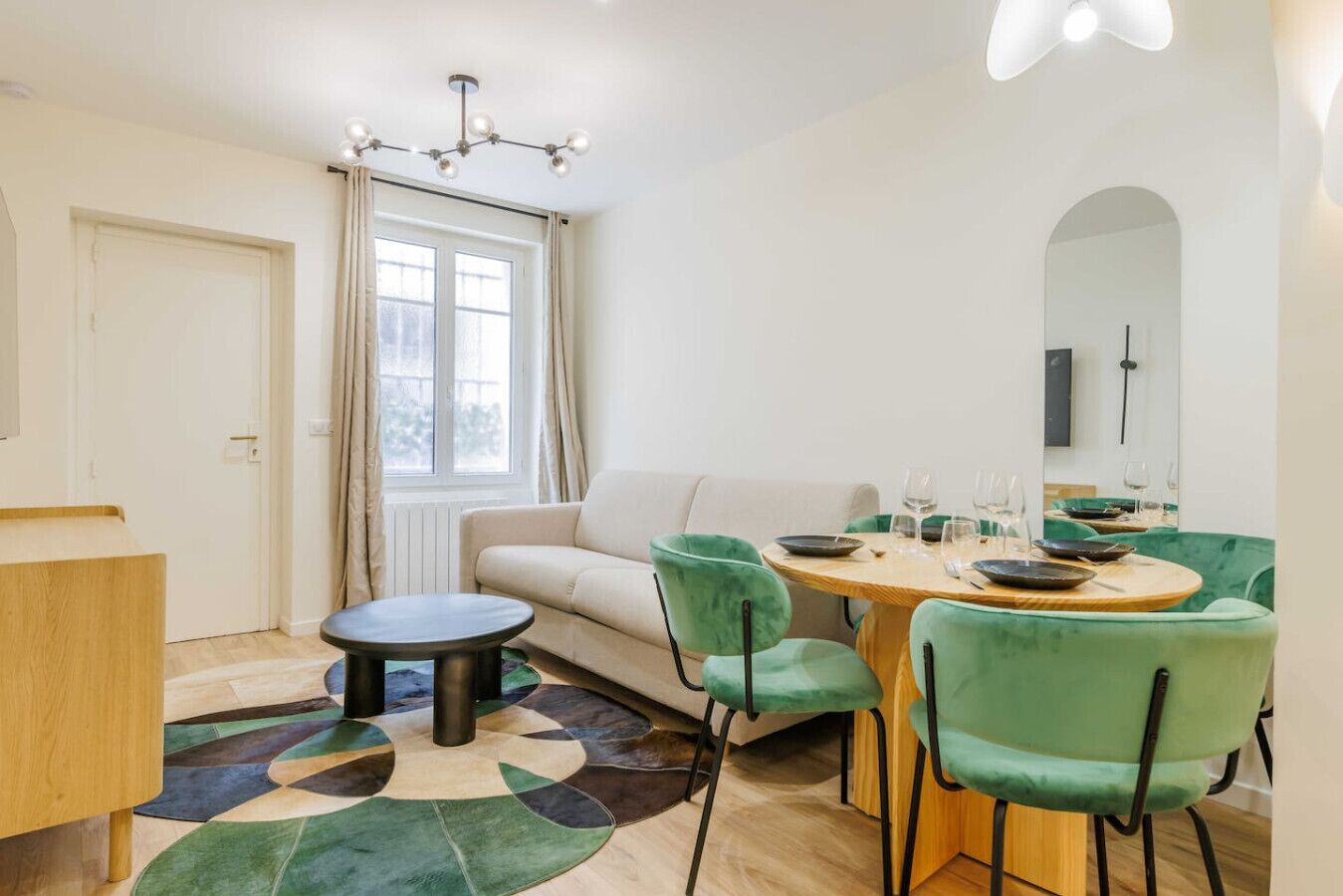A modern living room with a round dining table, green chairs, a sofa, and a large window with curtains.