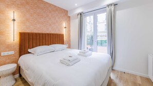 A modern hotel room with a large bed, a brick accent wall, and a view of the city through the window. - 2Bedrooms#6pers#Poissoniers#Paris 18#AC (Paris)