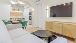 A modern living room with a sofa, a dining table with chairs, a TV mounted on the wall, and a kitchen in the background. - 2Bedrooms#6pers#Poissoniers#Paris 18#AC (Paris)