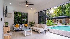 A modern living room with a pool, large windows, and a ceiling fan.